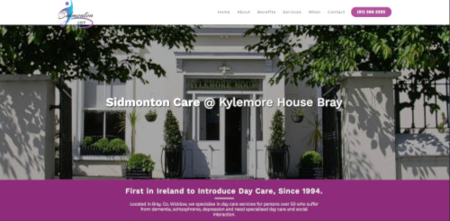 A white building with multiple windows and greenery, featuring the sign 'Sidmonton Care @ Kylemore House Bray.' The entrance has a welcoming pathway and plants on either side.